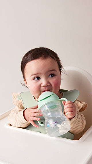 baby sitting in high chair drinking from sippy cup